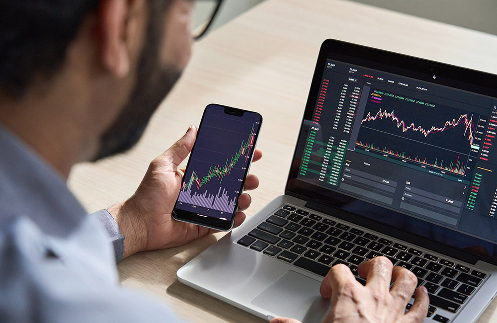 Trading online: come funziona Uomo che analizza grafici di trading online in tempo reale su smartphone e computer portatile